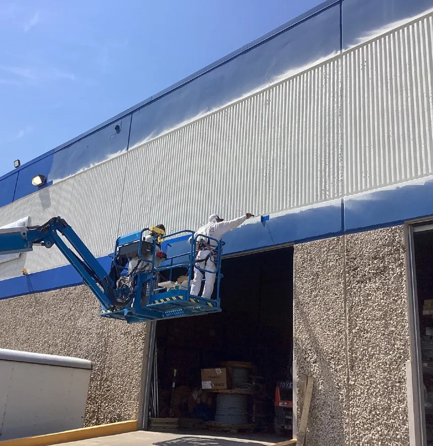 Painters on a boom lift coating a warehouse exterior